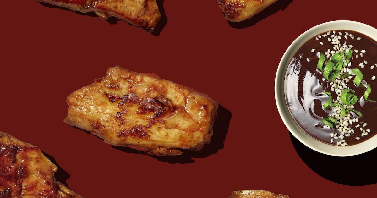 Pieces of Daring chicken and a bowl of sauce on a maroon background