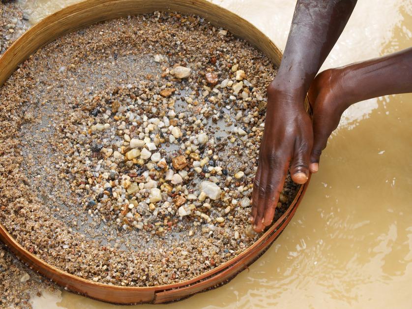 A person's hands sifting through dirt and rocks to find diamonds above a body of water. 