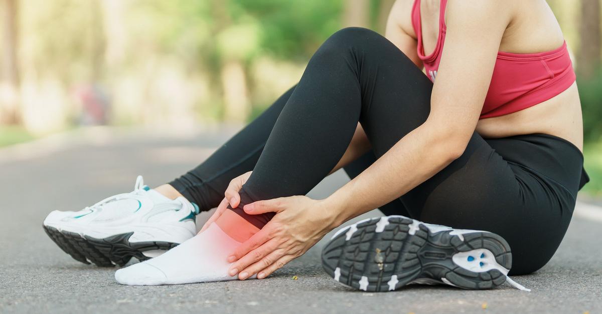 woman sitting in the road taking one of her running shoes off because she has Achilles tendonitis