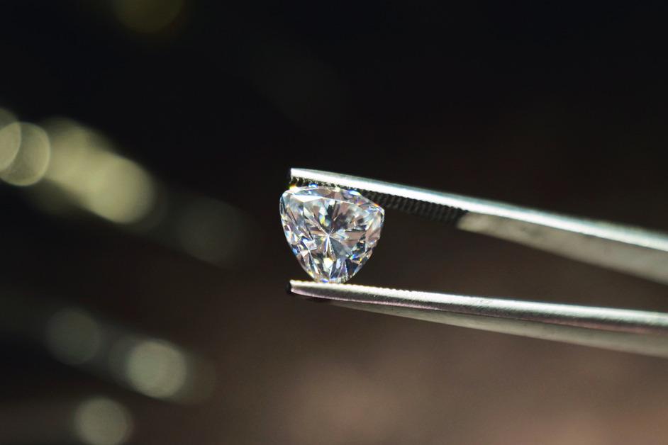 A close up of a pair of tweezers holding a shining diamond carat. 