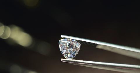 A close up of a pair of tweezers holding a shining diamond carat.