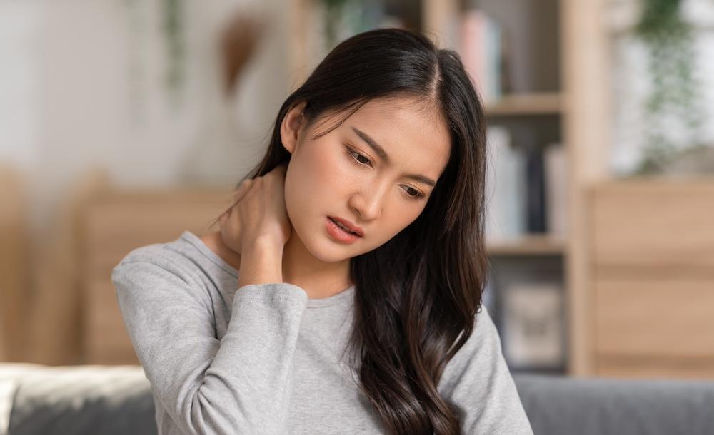 A woman looking down while she rubs her neck. 