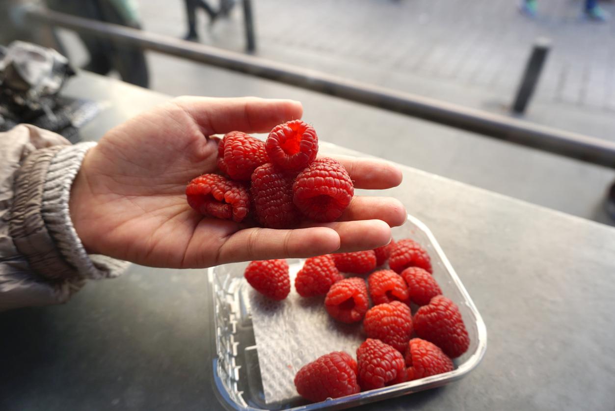 Person holding a few raspberries in their hand next to the rest of the container.