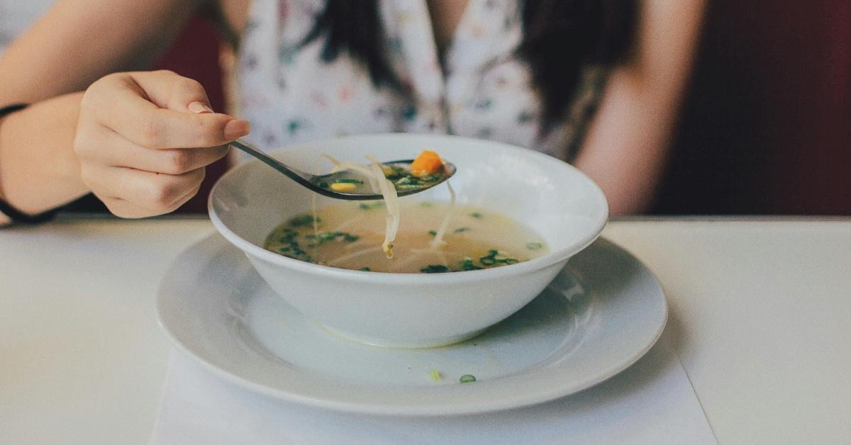 Young woman eating chicken noodle soup from a white ceramic bowl. 