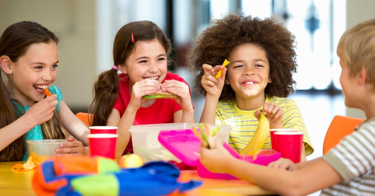 A group of children gather around a table to each healthy foods for lunch