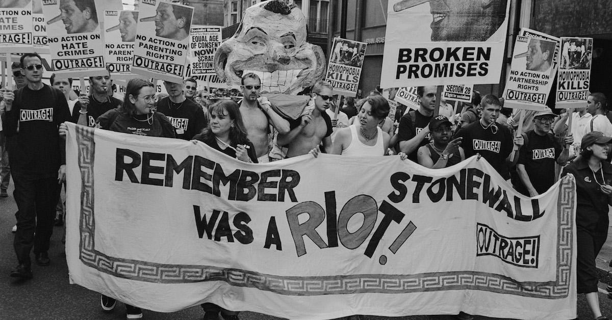 An archival, black-and-white photo of people carrying a banner reading "Remember Stonewall was a riot!"