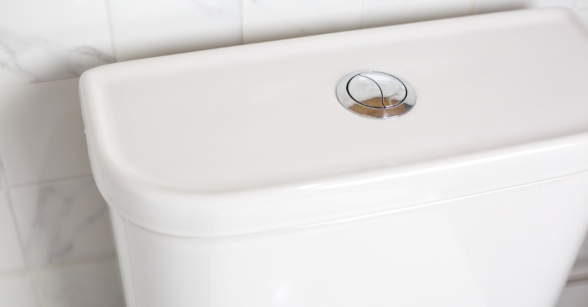 A closeup of a push-flush toilet tank