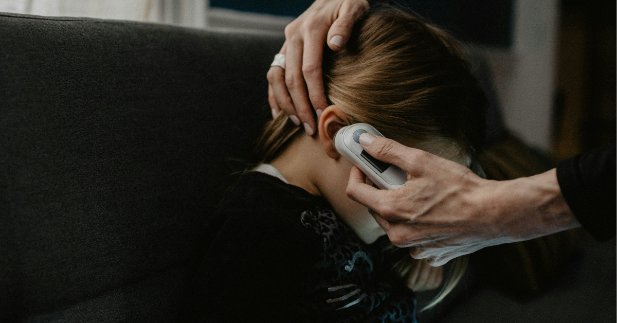 A mom puts a thermometer in her daughter's ear to read her temperature
