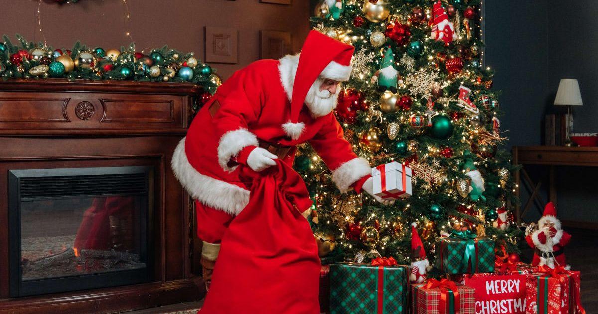 A man dressed as Santa Claus puts a gift under the Christmas tree. (Representative Cover Image Source: Getty Images | Alexander Dubynin)
