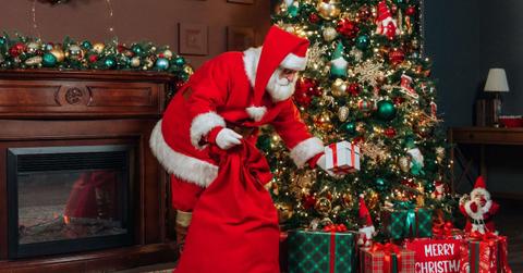A man dressed as Santa Claus puts a gift under the Christmas tree. (Representative Cover Image Source: Getty Images | Alexander Dubynin)