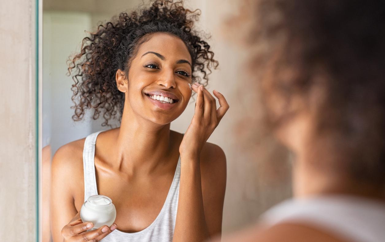 A woman applying face cream in a mirror. 