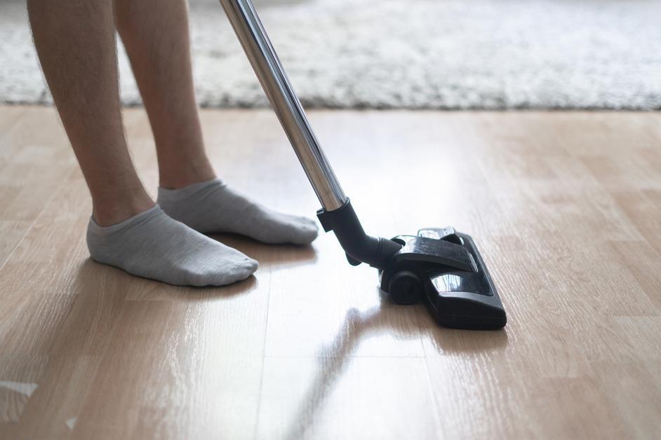 A person wearing gray socks uses a small vacuum on hardwood floors. 