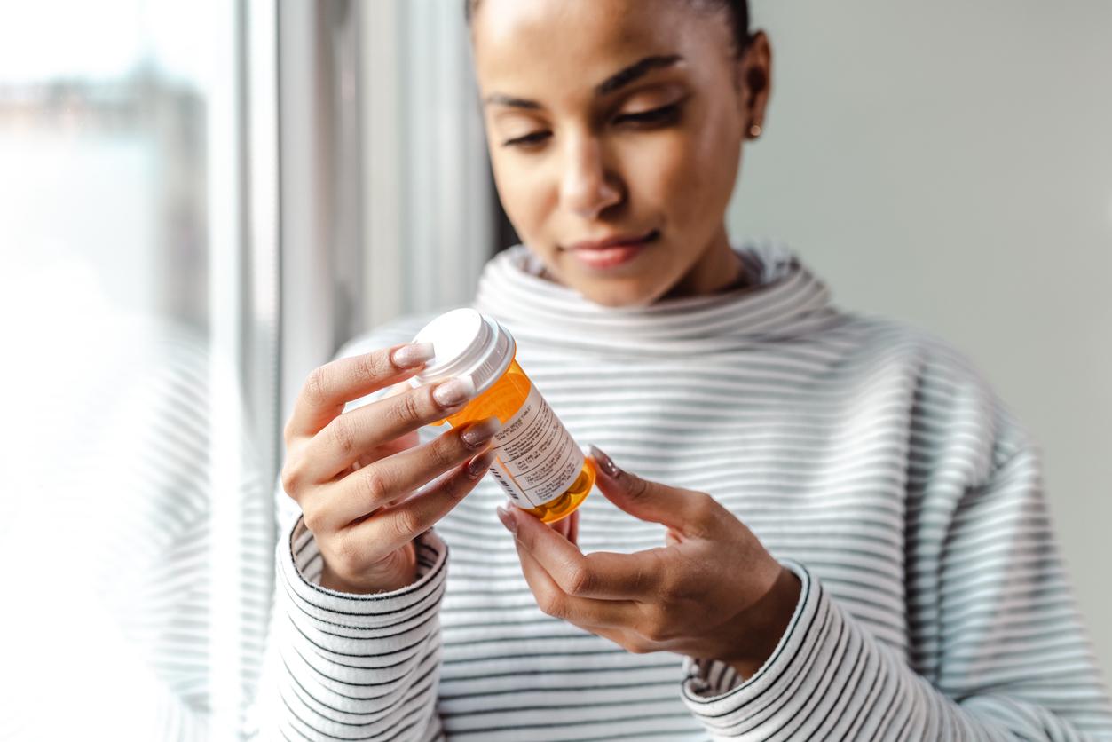 A woman looks at an orange pill bottle.