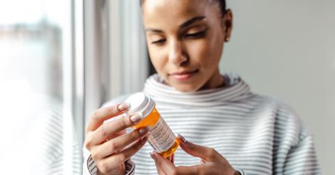 A woman looks at an orange pill bottle.