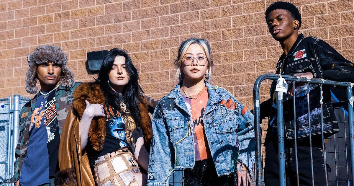 Four people wearing upcycled T-shirts and jackets model for the camera in front of a brick wall.