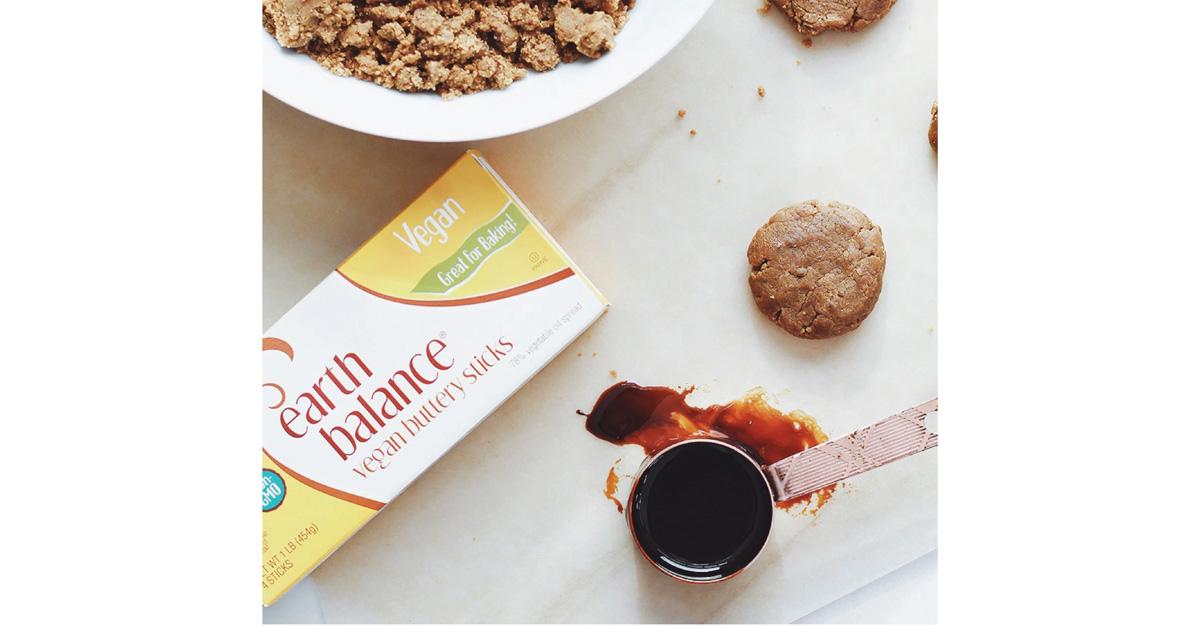 Earth Balance vegan butter sticks on a table with molasses in a measuring cup and cookie dough.