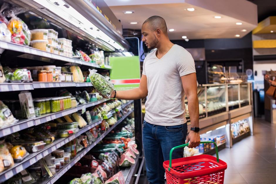 Man holding bag of vegetables in front of refrigerated food at the grocery store. 